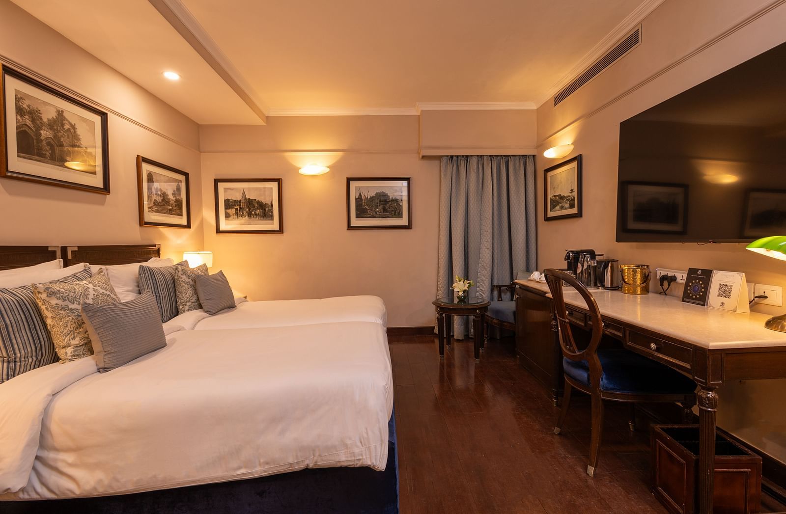 Side view of the Superior Twin Bed Room at The Claridges New Delhi, showcasing twin beds, a wall-mounted TV, and bedside lamps