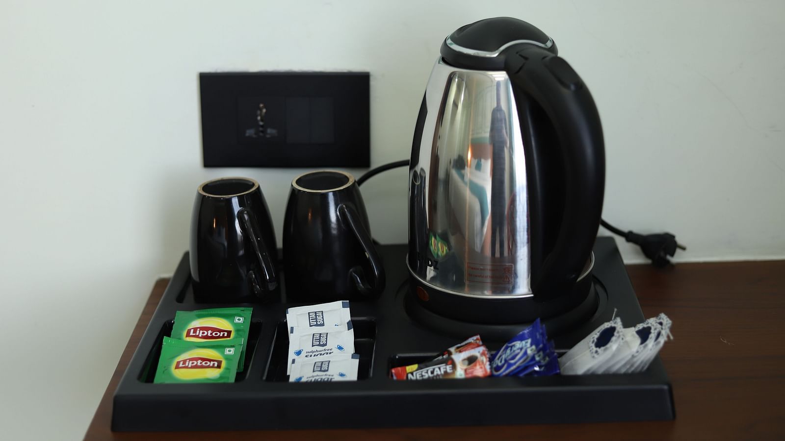 A kettle, cups, and sachets are presented on a tray next to a small screen - Asian Suites IFFCO Metro, Gurgaon
