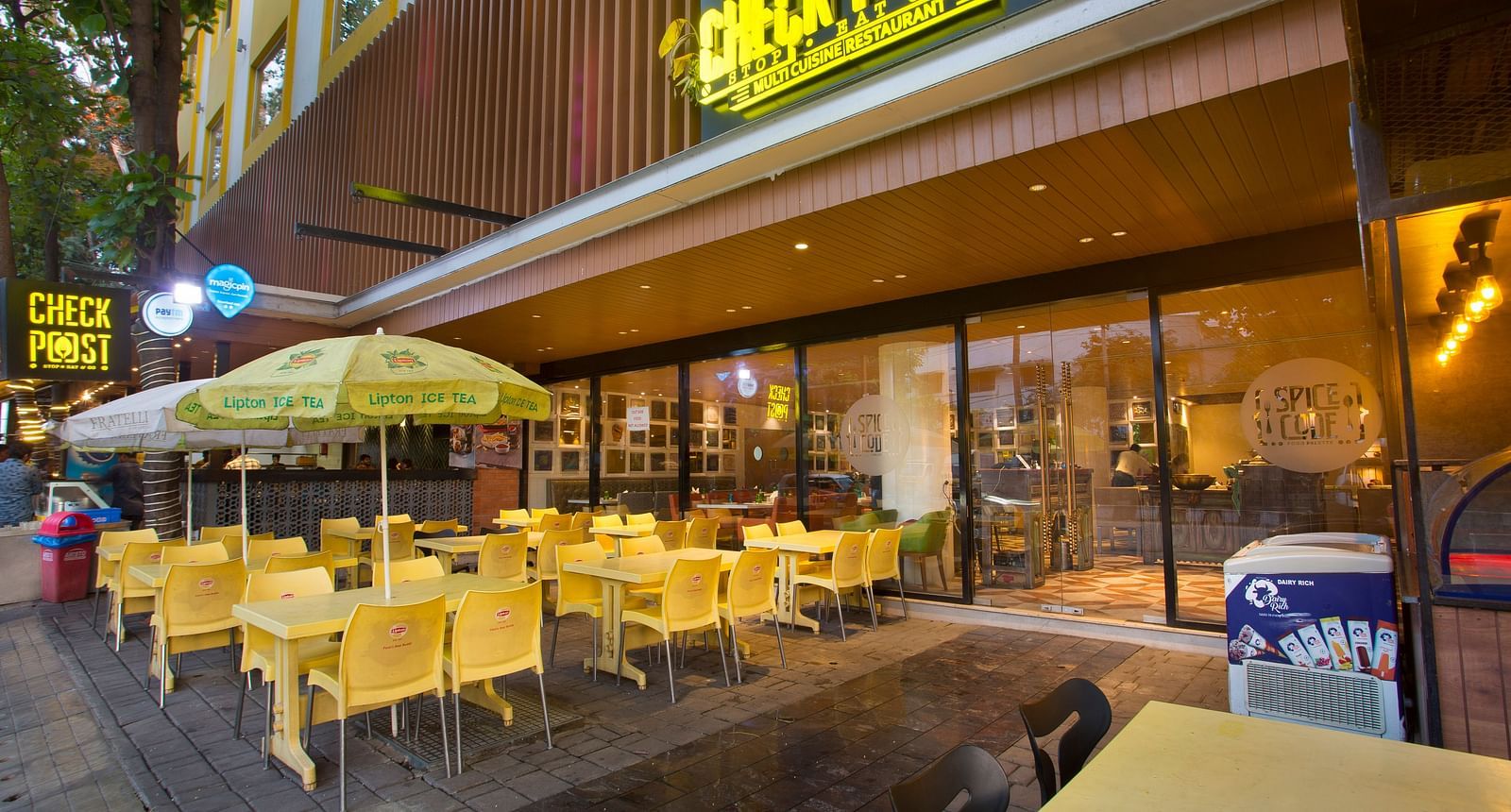 an outdoor restaurant with umbrellas mounted on the tables to provide shade - Hotel Fountain Tree By TGI - JP Nagar, Bangalore