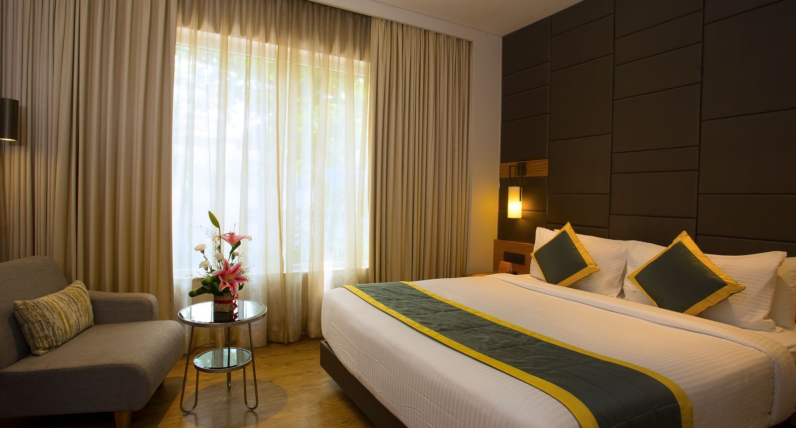 a bedroom with a large bed and a sofa opposite the the bed, with a small table in the middle - Hotel Fountain Tree By TGI - JP Nagar, Bangalore