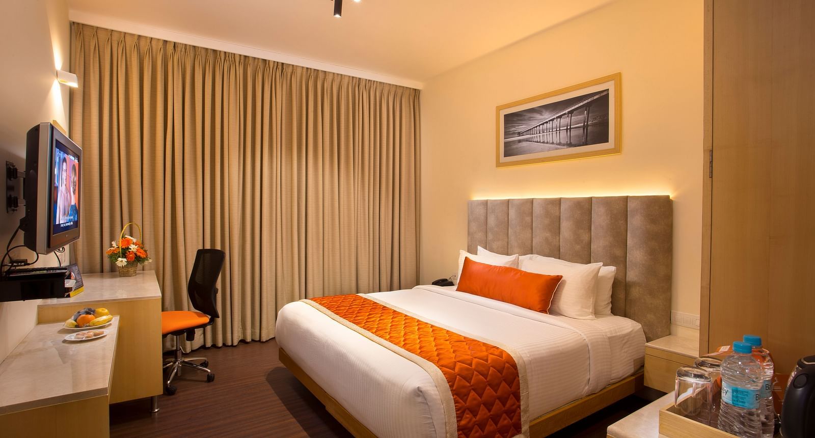 A cosy hotel room with a plush bed adorned with an orange bed runner, a work desk and a wall-mounted TV - Hotel Langford Keys by TGI, Shanti Nagar