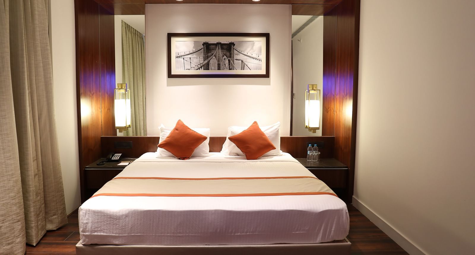 The front view of a hotel room with a large bed, white linens, burnt orange accents and a framed picture of a bridge above the headboard - Hotel Southend by TGI - Bommasandra, Bangalore