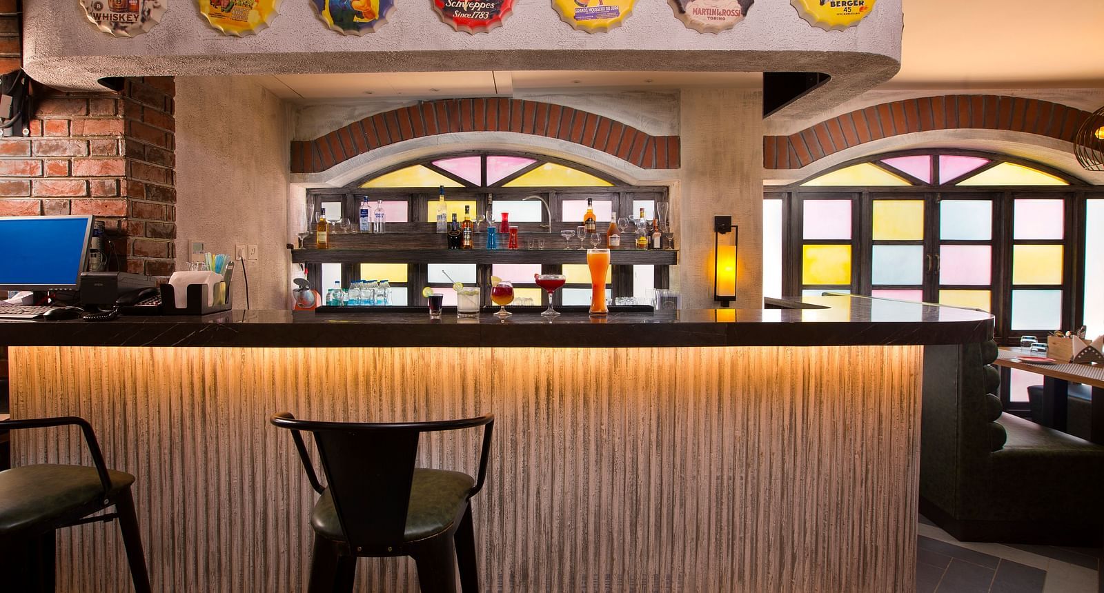 A stylish bar with colourful stained glass windows, a variety of drinks on display and vintage advertisements on the wall - Hotel Southend by TGI - Bommasandra, Bangalore