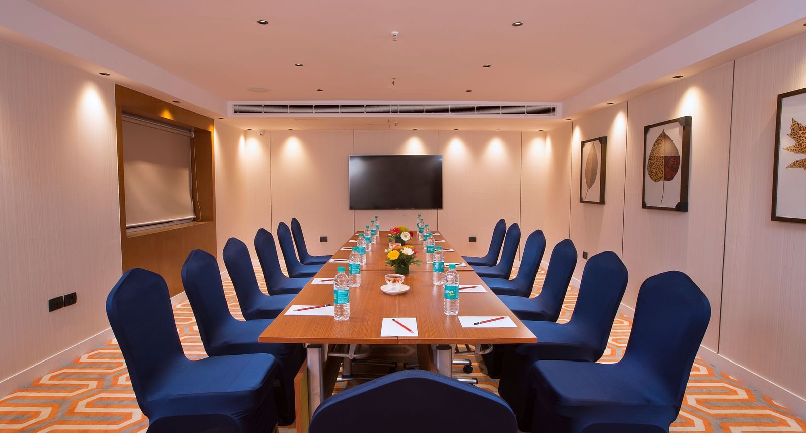 A well-lit boardroom with a long table, blue chairs and a large screen on the wall, suitable for business meetings - Hotel Southend by TGI - Bommasandra, Bangalore