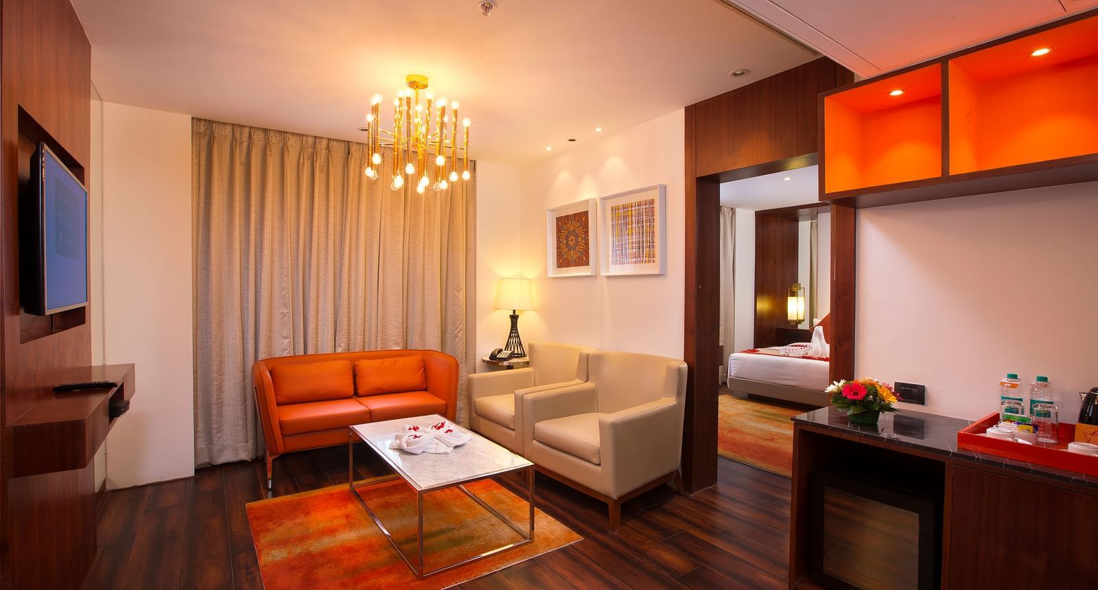 A hotel suite living area with a modern chandelier, orange leather sofa and a marble coffee table - Hotel Southend by TGI - Bommasandra, Bangalore
