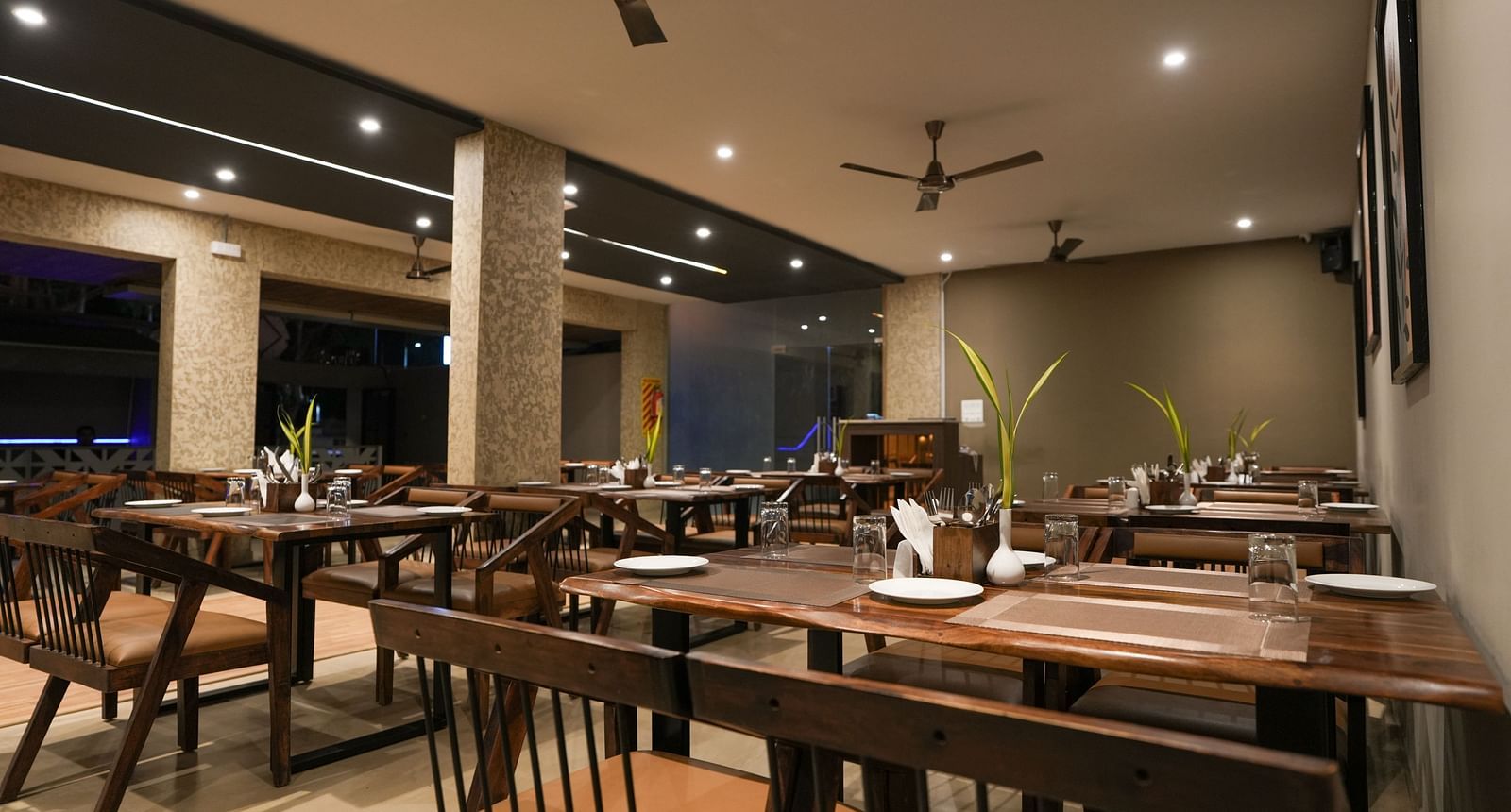 Evening restaurant view with ceiling fans, spotlights, and wooden dining furniture at TGI Livancia Hillside, JC Nagar, Mysore