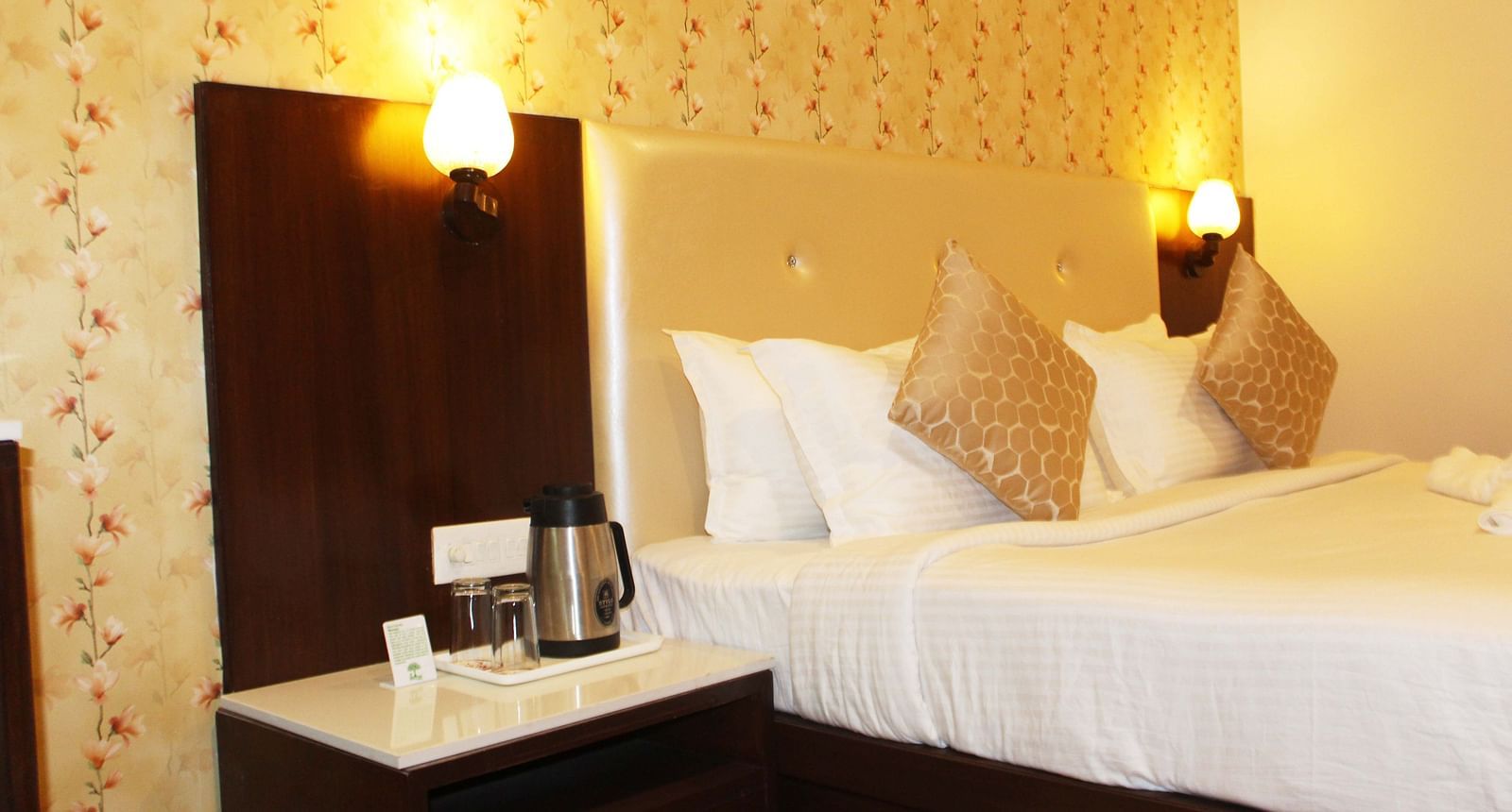 A hotel room with a beige headboard, white linens, floral wallpaper and a coffee-making station - TGI Apple Inn, Jaipur 