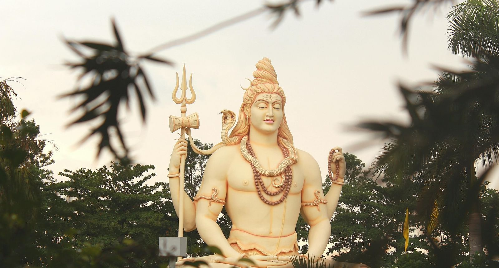 image of a white coloured statue of lord shiva standing tall surrounded by greenery