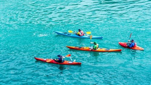 an images showing a group of four people kayaking in blue azure waters 