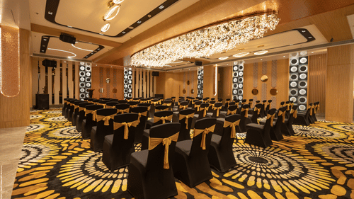 A well-lit banquet hall featuring rows of chairs with black and yellow covers and an linear chandelier | Pride Elite Chhatrapati Sambhajinagar