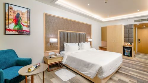 Junior Suite with king bed, accent chair, and wall art at Sarovar Portico, Ajmer.