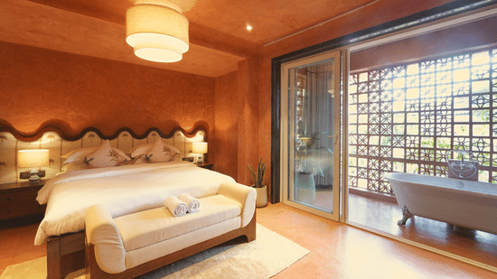 A room at Unseen Boutique Hotel Assagao Goa featuring a king bed with white bedding a wooden bench warm terracotta walls a pendant light and a glass door leading to an outdoor bathtub area.