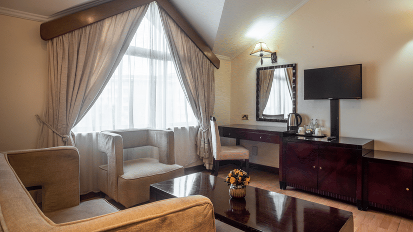 Living room of Suite at Boma Inn Nairobi featuring a sofa set placed in L shape by the window with a coffee table and one facing the TV on the wall next to a mirror