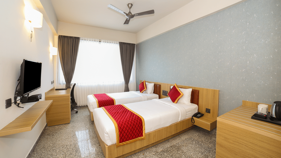 Two single beds, a wall-mounted television, and a wooden desk at Icon Express By Bhagini, Hoodi.