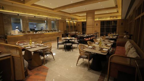 A spacious dining area with set tables and chairs and a buffet arranged in the background. - Heritage Village Resorts & Spa 