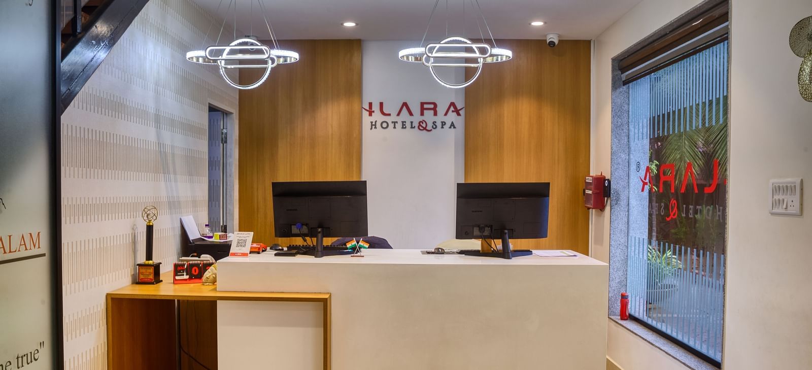 The well-lit and modern reception desk, featuring two computer monitors and clean wooden accents at Ilara Hotels & Spa, OMR, Chennai.