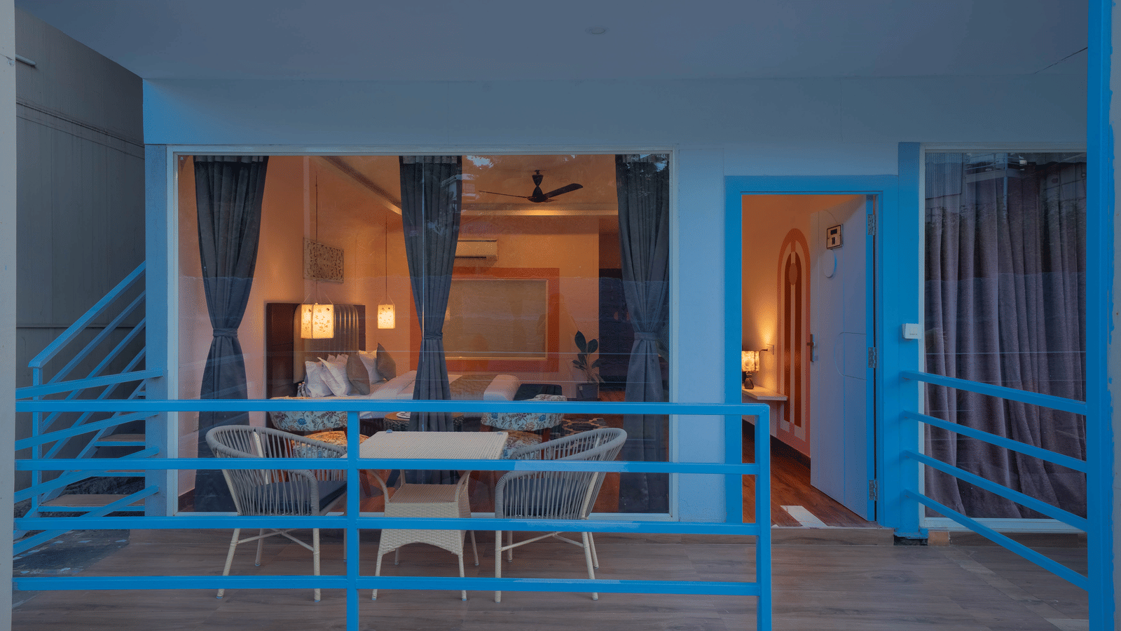 A balcony with blue railings, a seating area featuring 2 chairs and a coffee table, and a glimpse of the room behind it - Perfectstayz Koko Maya