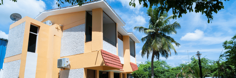 Image of a two-storey building painted in coral and white with pavements in front of it on a sunny day