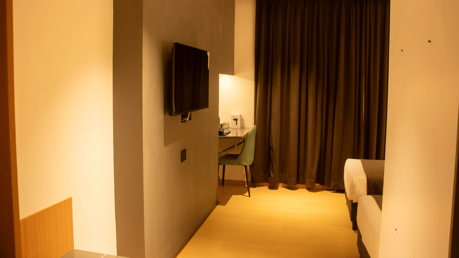 A bedroom with wall-mounted TV, desk, chair, 2 single beds, and closed curtains at Magnus Lxia Premier, Kalyani Nagar.