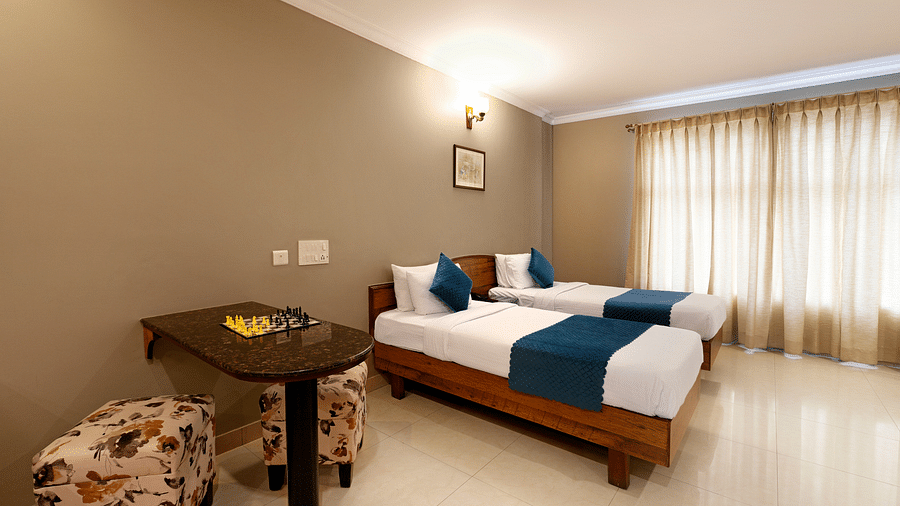 A Deluxe Room with a desk, twin beds, and bright natural light coming from the window - Cross Roads Inn, Bengaluru