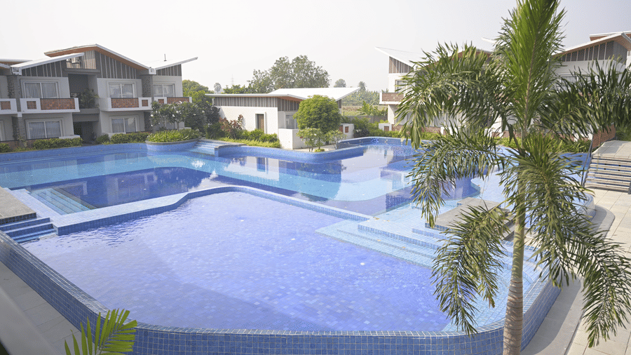  An outdoor blue swimming pool surrounded by hotel buildings and a palm tree at Hotel Sonar Bangla, Mayapur.