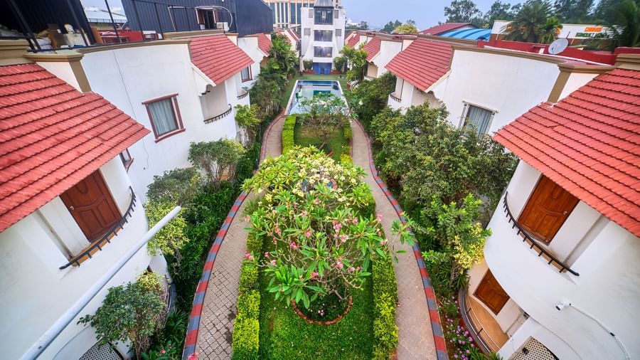 Elevated view showcasing a row of villa-style accommodations with striking red tiled roofs and lush green pathways between them at Ilara Hotels & Spa, OMR, Chennai.