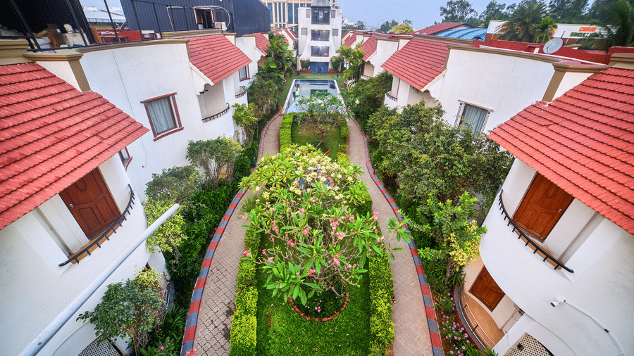 Elevated view showcasing a row of villa-style accommodations with striking red tiled roofs and lush green pathways between them at Ilara Hotels & Spa, OMR, Chennai.