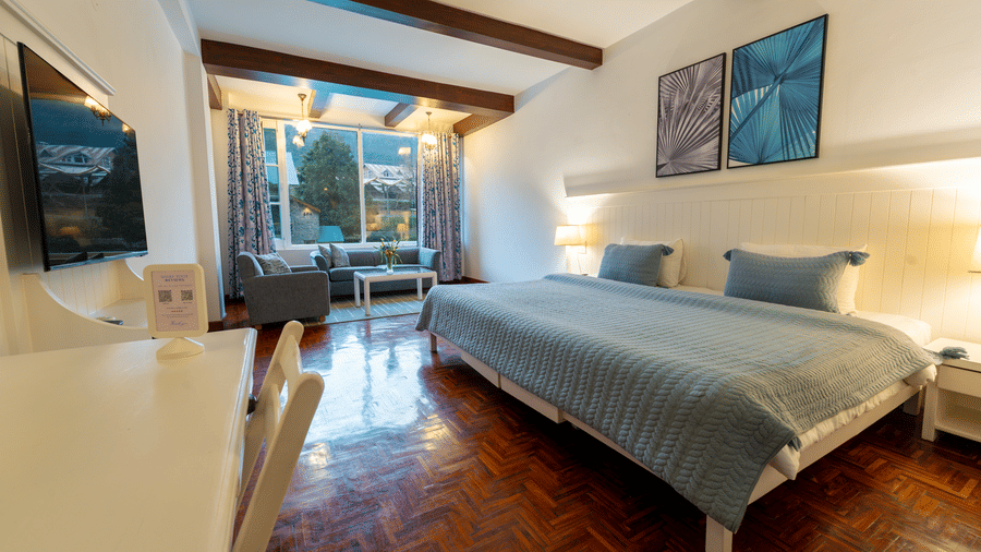 A spacious premium suite featuring light blue bedding, wall-mounted TV, and bright natural light - Johnson Lodge & Spa, Manali