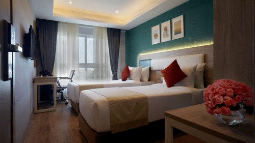 view of twin beds, a side table with a vase, a television, and a work desk and chair inside one of the deluxe rooms at Sarovar Portico, Kolkata Rajarhat