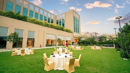 An elegant outdoor event space with round tables set up on a lush green lawn, adjacent to the hotel