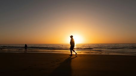 Silhouette of a man walking on a beach side and there is sun setting at the horizon.