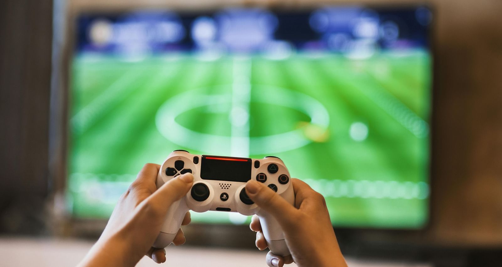 a person holding a play station controller with a huge television screen with a football game