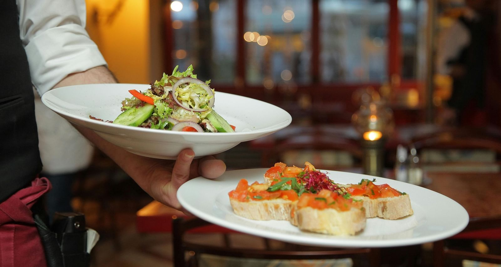 a person in a restaurant holding two plates with delicious cuisines in it that are well plated