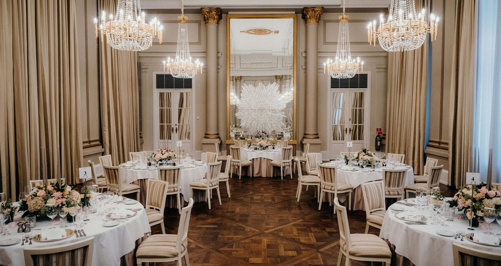A grand ballroom featuring multiple round tables with linens and warm lighting