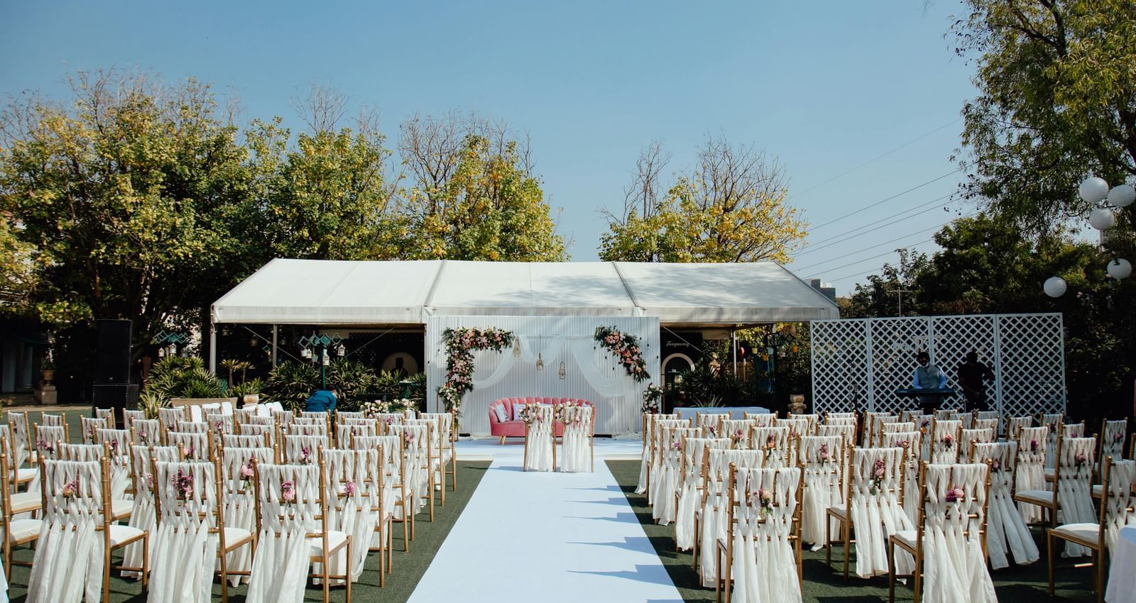 Wedding aisle with chairs and a stage under a canopy in an open lawn.