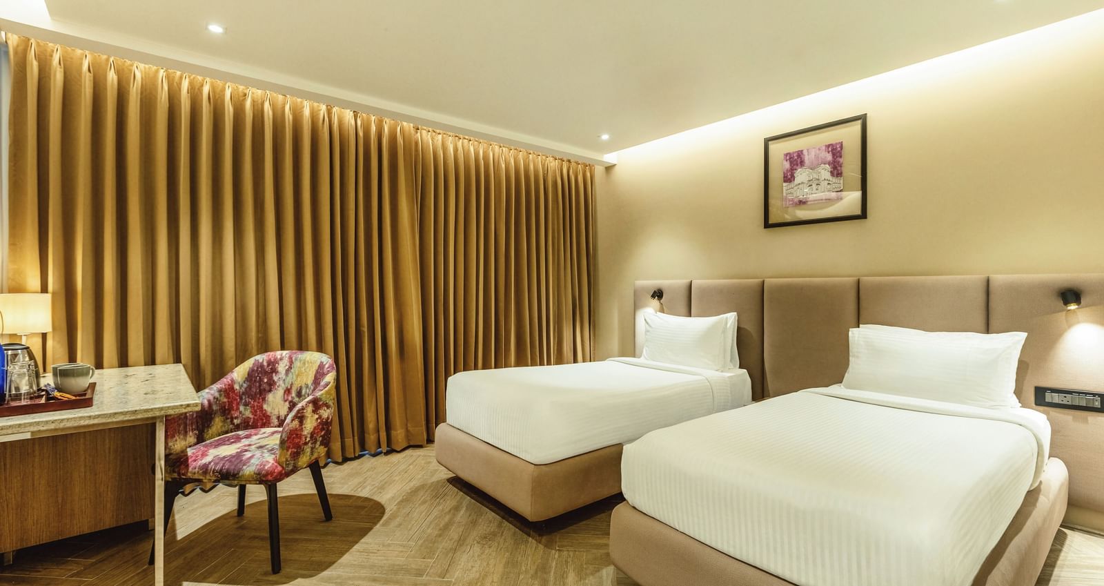 A wide shot of a twin-bedded room at Mango Hill Central, Chennai. A desk is on the left, and a wooden slat wall is behind the beds.