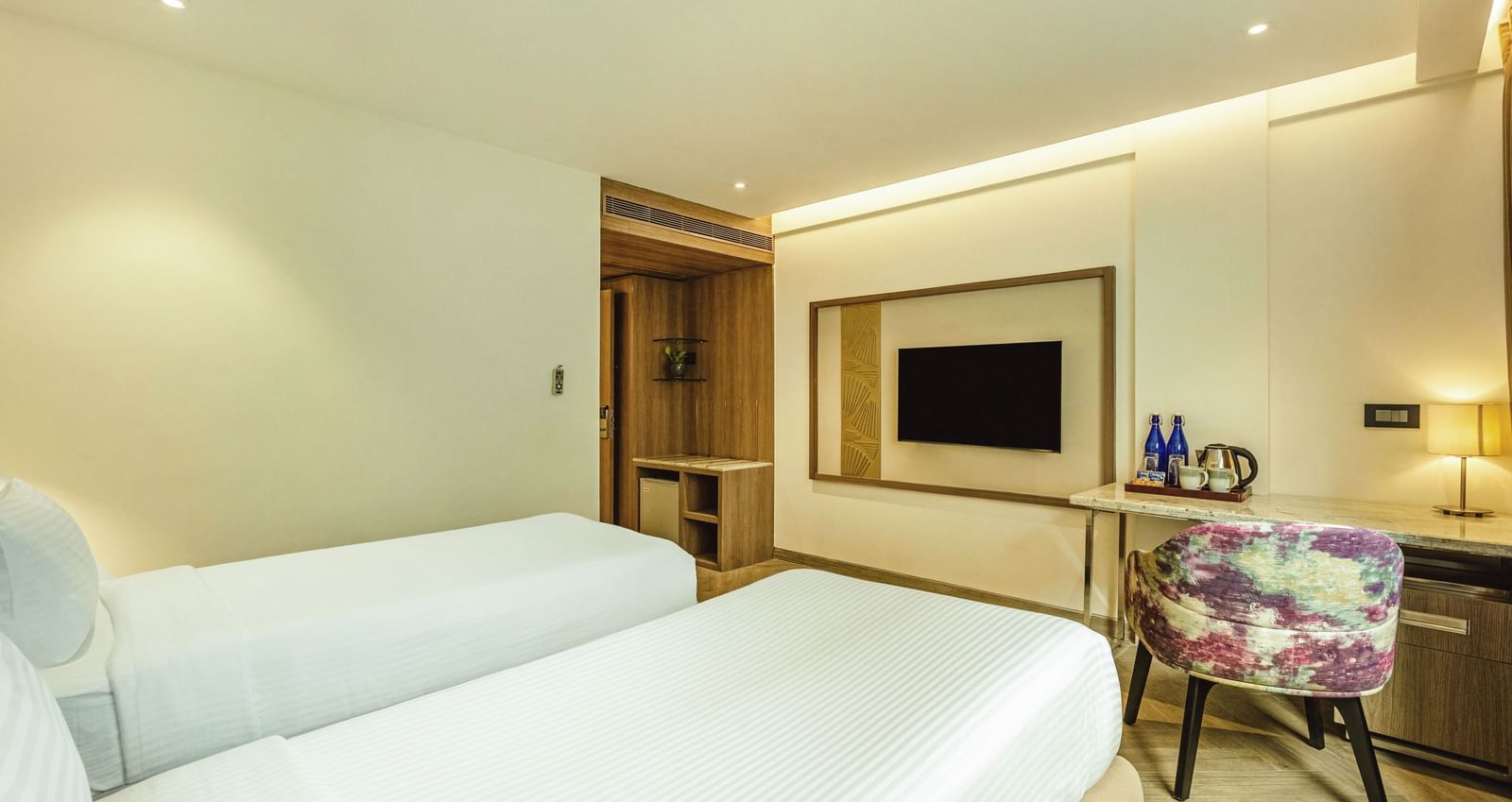 A twin-bedded room with a television and a desk, seen from an angle, at Mango Hill Central, Chennai.