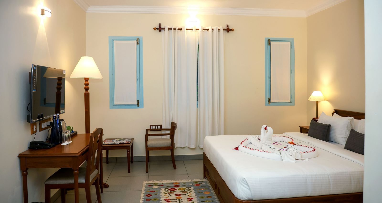 A suite with a large bed, flat screen TV, table and chair, and three lamps of different sizes | Mango Hill La Serene, Pondicherry