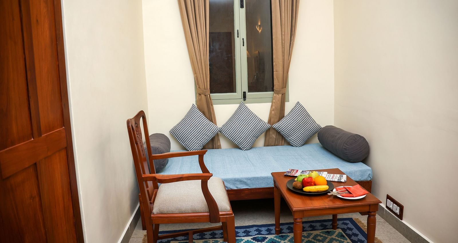 A sitting area with sofa, cushions, wooden chair and a centre table | Mango Hill La Serene, Pondicherry
