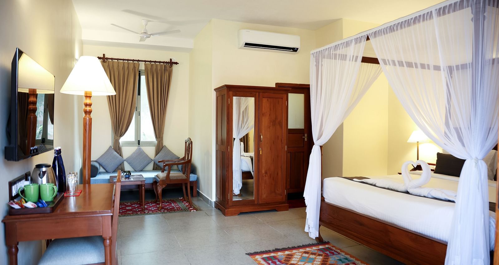 A room that has a poster-bed, a cupoard, sitting area, table and chair, etc.A sitting area, a cupboard, and a tall lamp | Mango Hill La Serene, Pondicherry