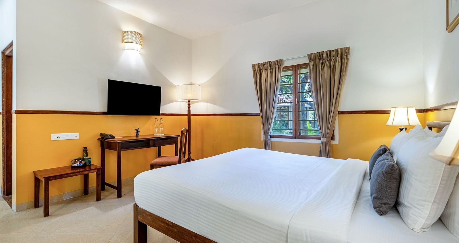 Well-lit bedroom with a wooden bed frame, white linens, a desk and chair, a flat-screen TV, and a window with drapes| Mango Hill Shallow Beach Resort ECR