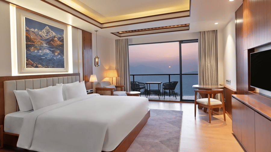 An Executive Room at Royal Tulip Shivapuri National Park - Kathmandu featuring a white king bed, mountain artwork, and a balcony with a sunset view.