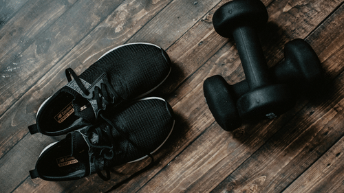 Black athletic shoes and dumbbells resting on a wooden floor