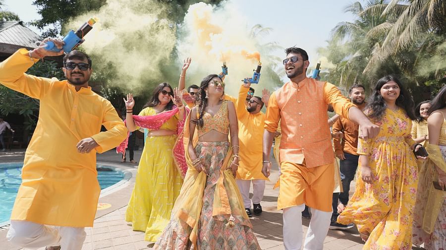 An image of an outdoor celebration with guests dressed in bright traditional attire, holding smoke guns releasing smoke, dancing and having fun near a pool
