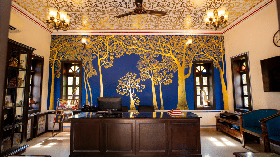 A reception counter sitting before a blue wall featuring gold tree art under ornate ceiling patterns at Garh Govind.
