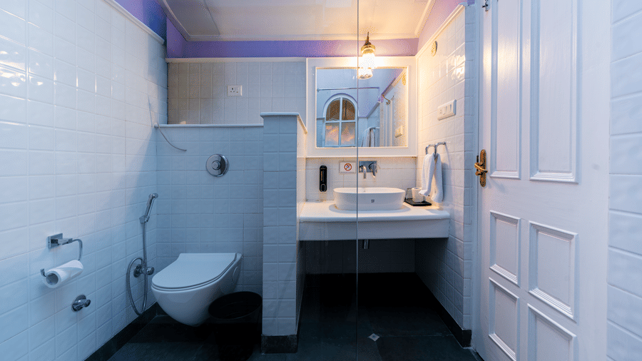 A crisp, white en-suite bathroom with a wall-mounted toilet, vessel sink, and purple ceiling accents - Johnson Lodge & Spa, Manali