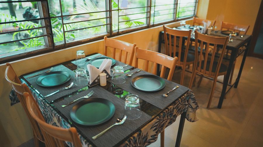 A dining table with green plates set up next to a large window overlooking greenery.
