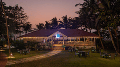 The exterior facade of Kai, the seaside restaurant that looks enchanting in the late evening sky with a walkway leading to the restaurant and trees surrounding the exterior at Kenilworth Resort & Spa, Goa.