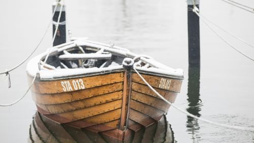a wooden boat tied on to two wooden logs to not let it wander on the river