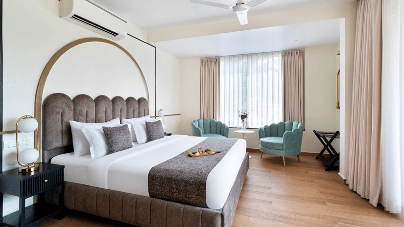 A daytime image of a room featuring a bed, two sofa chairs, a coffee table, a side table with a lamp, and a ceiling fan.